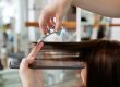 Close up of beautician s hand with a comb cutting hair of woman