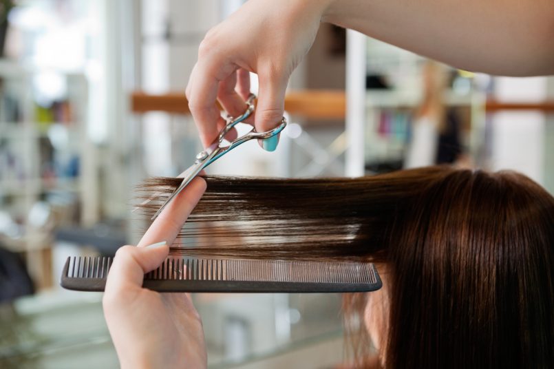 Close up of beautician s hand with a comb cutting hair of woman