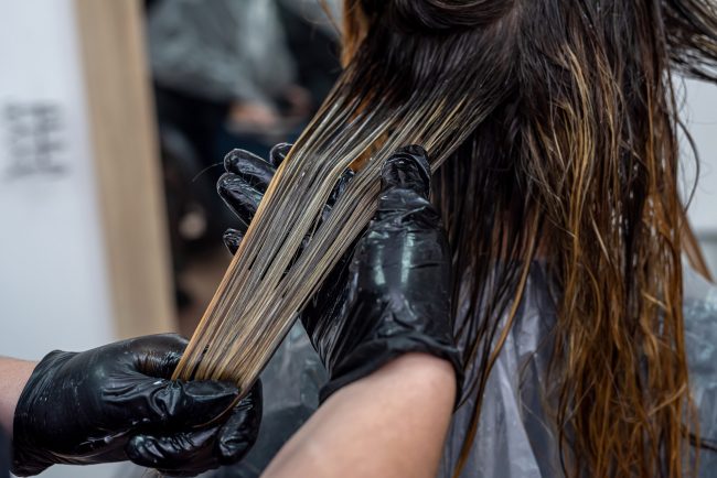 200027751_m beautiful young brunette girl sitting on the procedure of hair coloring